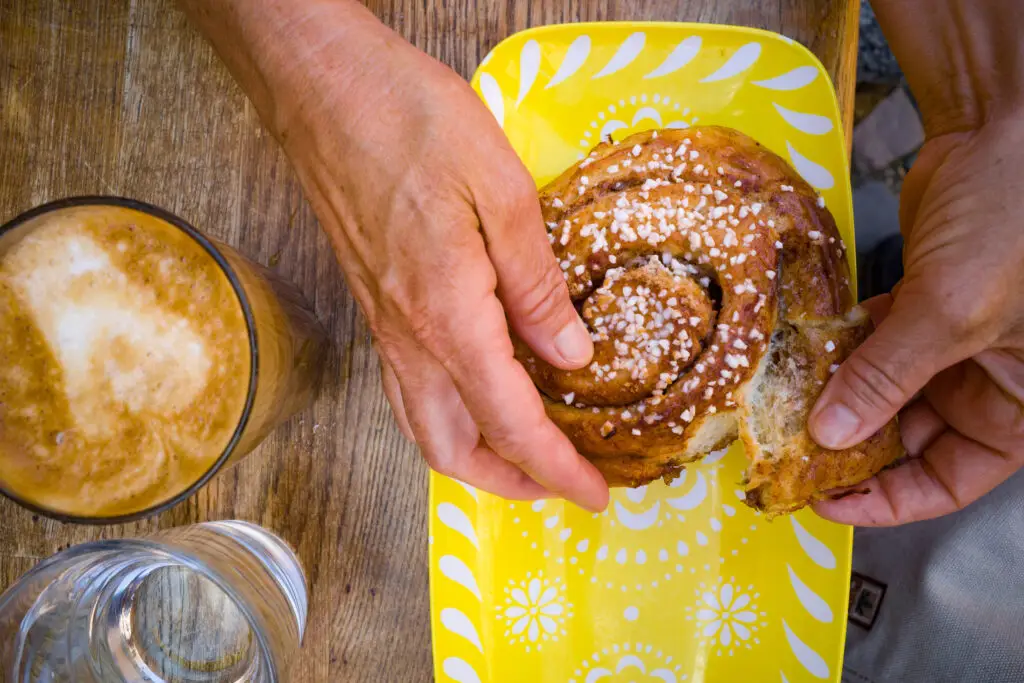 Enjoying a traditional Swedish fika with a cinnamon bun and cafe au lait on a yellow plate, Gothenburg, Sweden