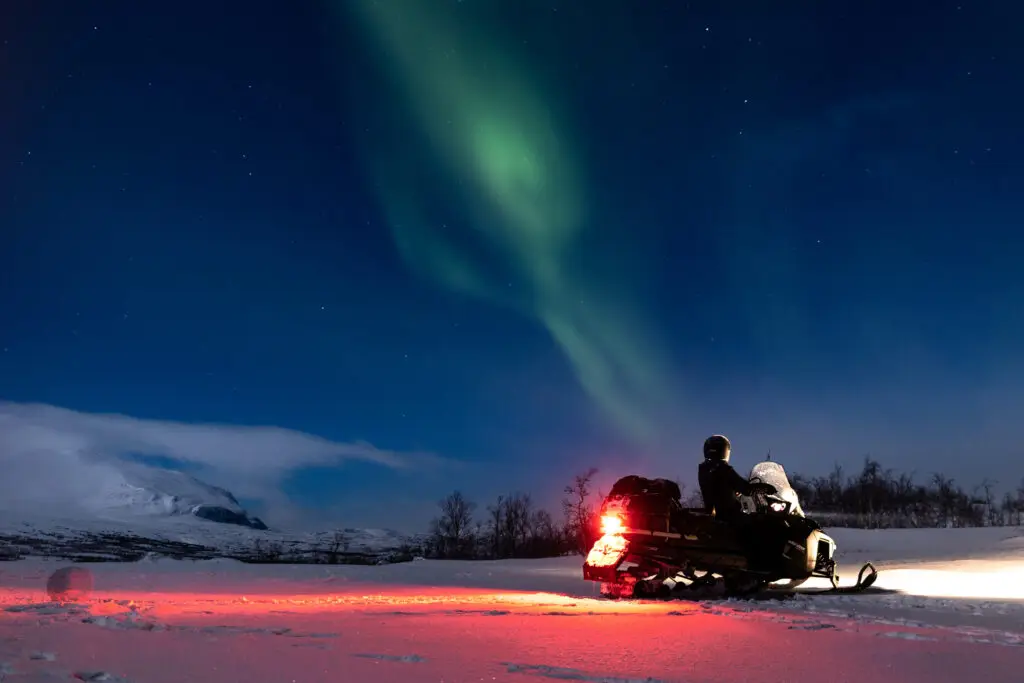 Snowmobile under the vibrant northern lights in a Scandinavian winter landscape.