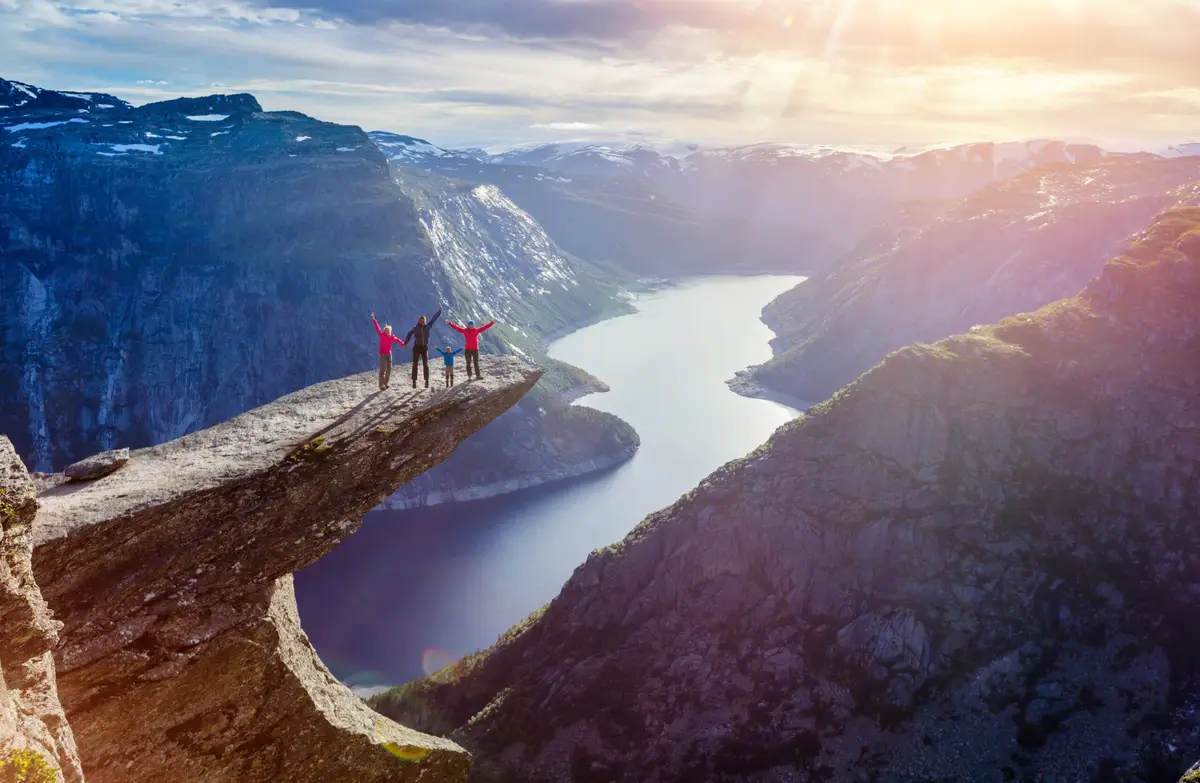 Family enjoying a scenic view on Trolltunga cliff over Ringedalsvatnet lake during a tour in Norway.