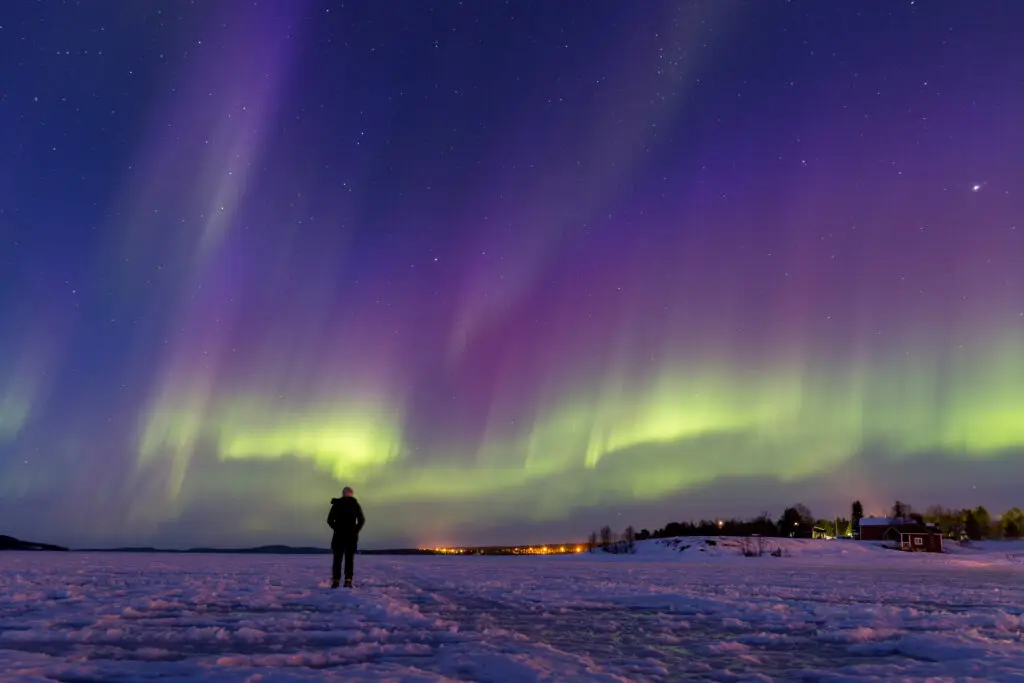 Person standing on frozen Lake Inari under a vibrant display of Northern Lights in Finland