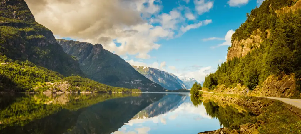 Panoramic view of Hardanger Fjord in Norway showcasing serene waters, lush green hillsides, and a clear sky reflecting on water, perfect for tourism and nature exploration.