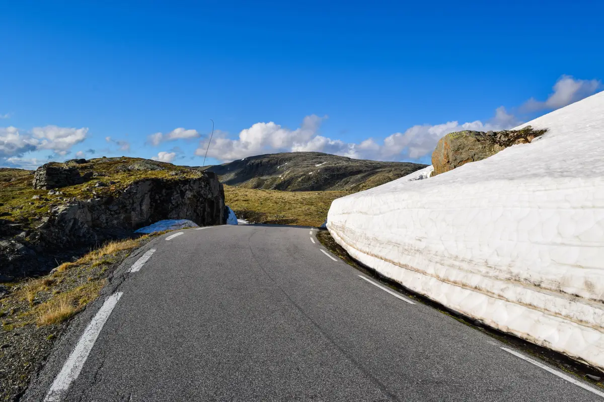 Scenic view of the snow-covered National Tourist Route Aurlandsvegen in Norway with open road and clear blue sky.