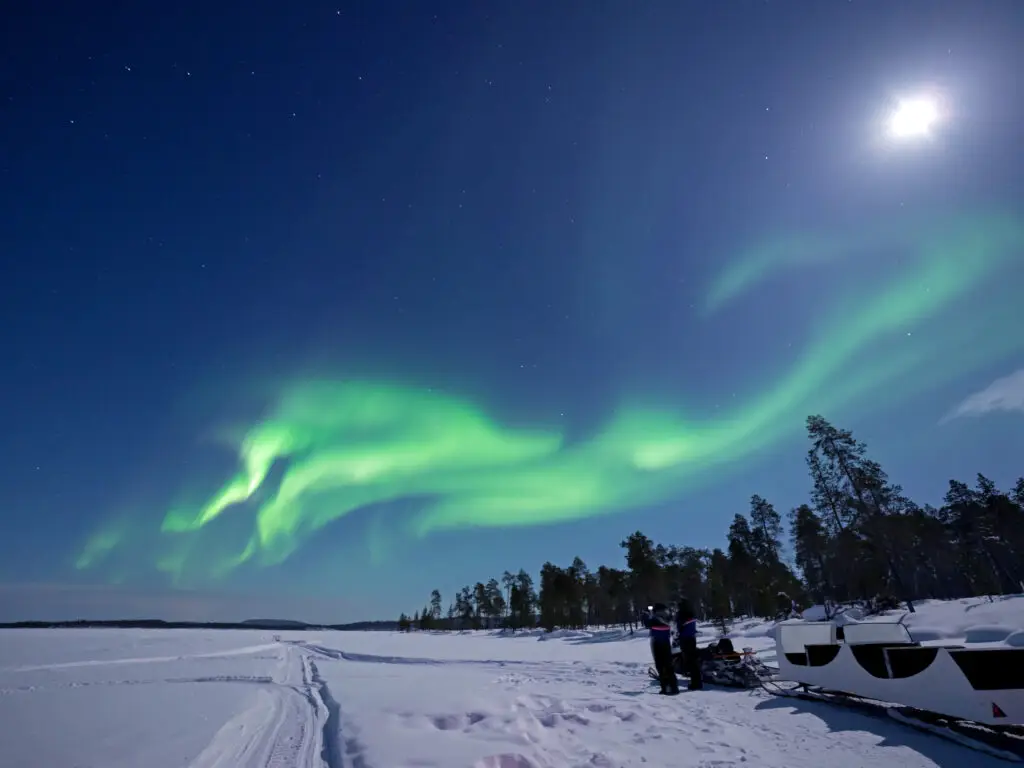 Aurora Borealis dancing over the snowy landscape of Lake Inari, Finland, with snow-covered boats and starry night sky