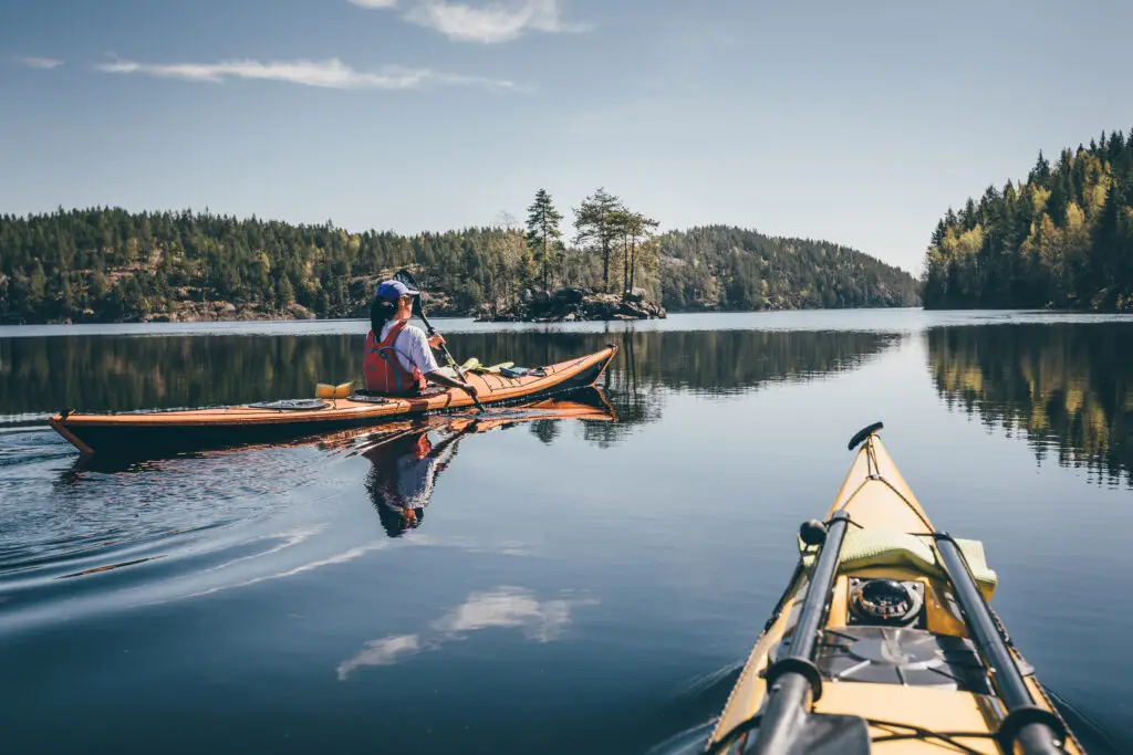 Person kayaking on a serene Finnish lake surrounded by forest during summer, perfect for exploring Finland's natural beauty.