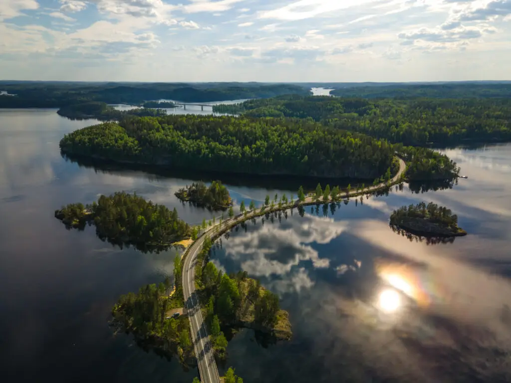 Aerial view of a serene Lake Saimaa in the Puumala Lakeland region, Finland, showcasing lush green islands and a curving road.