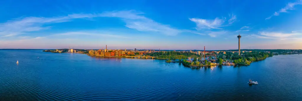 Aerial view of Särkänniemi amusement park in Tampere, Finland showcasing a vibrant sunset over the scenic lake with a towering observation tower and various attractions.