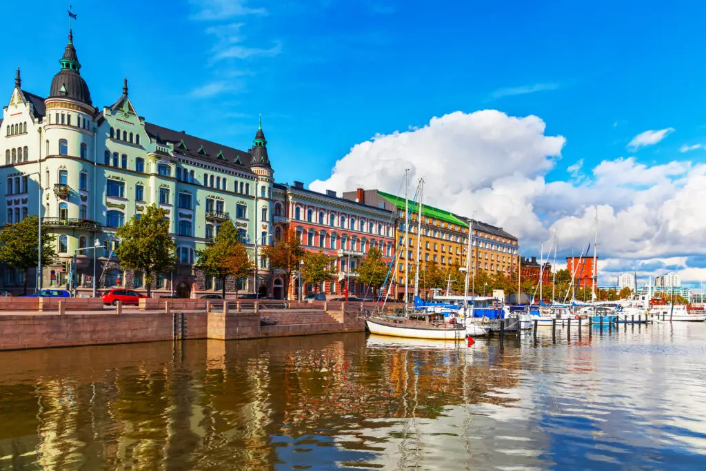 Colorful historical buildings and boats moored at Old Town pier in Helsinki, Finland, under a blue sky with puffy clouds.